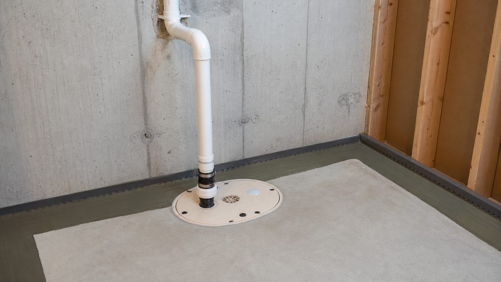 Clean sump basin and PVC discharge detail in an unfinished basement mechanical area